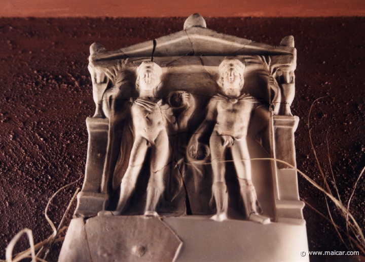 6915.jpg - 6915: Dioskurerna. Votivrelief i terrakotta. De båda dioskurerna Castor och Pollux avbildas i heroisk nakenhet förutom mantlarna som täcker deras axlar. I handen håller de varsin offerskål, phiale. Dioskurerna avbildas ofta inramade av en dörr karm. Reliefen var upphängd på en kultplats för Dioskurerna i Taranto. Ca 350 f.Kr. (Inv. nr. 4109). Medelhavsmuseet, Stockholm.