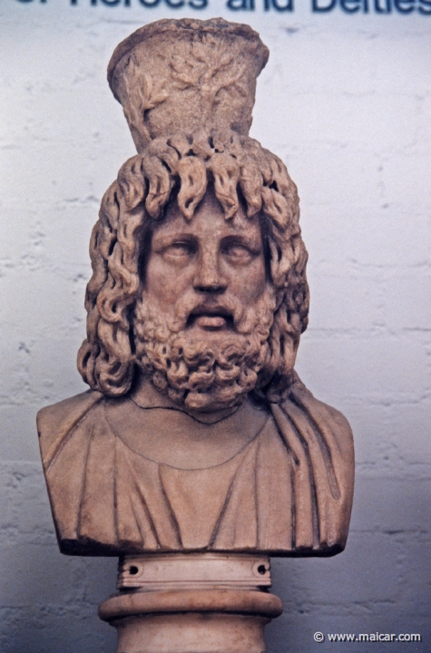 8022.jpg - 8022: Head from a statue of Jupiter Serapis, wearing a Kalathos (basket used in religious processions) decorated with olive branches. Marble, 2nd century AD. British Museum, London.